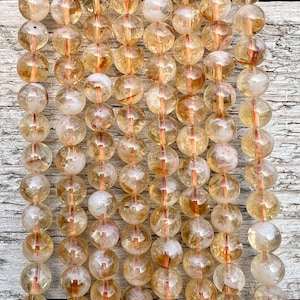 Może przedstawiać: Szereg okrągłych, przezroczystych, złotożółtych koralików z inkluzjami. Korale są nawleczone na drut i mają średnicę około 10 mm.