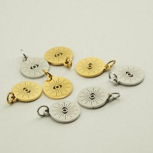 May include: A collection of gold and silver-colored round pendants. Each pendant features a central eye design with radiating lines. The pendants have small loops for attaching to a chain or bracelet. The pendants are likely for jewelry making.