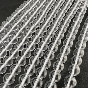 Op de afbeelding: Een streng van heldere kristallen kralen, elke kraal is rond en glad. De kralen zijn in rijen gerangschikt, waardoor een herhalend patroon ontstaat.