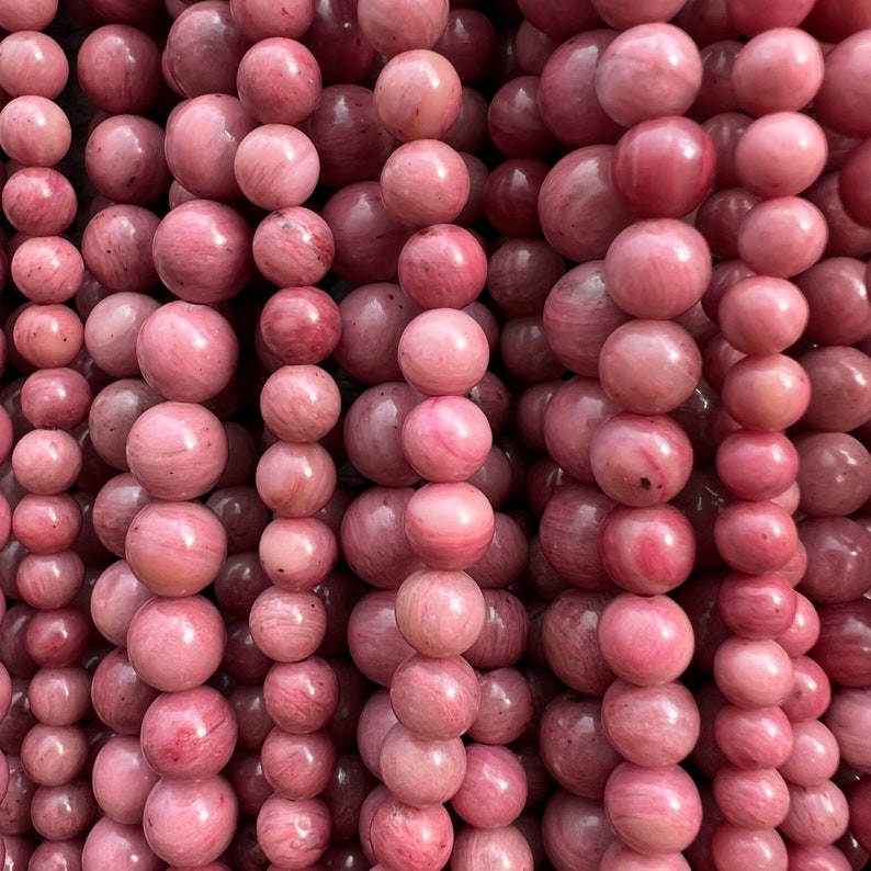 Rhodonite beads strands laid on a bright wooden board in outdoor under natural light. These are round 8mm beads with 1mm hole in middle for threading. they have a very delicate vein on them.