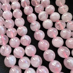 Madagascar rose quartz beads strands laid on a black background. these beads have a pink color with withe hues.