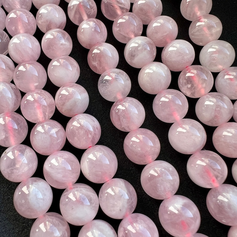 Madagascar rose quartz beads strands laid on a black background. these beads have a pink color with withe hues.