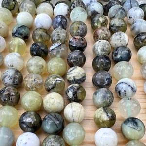 Puede incluir: Una colección de piedras preciosas redondas y pulidas en tonos verdes, blancos y grises. Las piedras tienen un aspecto veteado, con patrones y texturas variables. Las piedras preciosas están dispuestas muy juntas, llenando el marco.