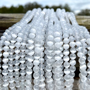 Selenite gemstone strands laid on a pieces of wood in outdoor and photographed under natural light. These beads are semi transparent with some white hues. Selenite beads have chatoyancy effect.