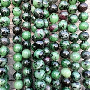 Könnte beinhalten: Eine Kette aus grünen und schwarzen Edelsteinen. Die Perlen sind rund und haben eine gesprenkelte Oberfläche.