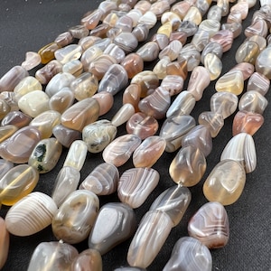 Può includere: Fili di perline di agata burattate nei toni del grigio, marrone e crema. Le perline hanno una finitura liscia e lucida e variano per dimensioni e forma. Le perline di pietra naturale sono infilate, pronte per la creazione di gioielli o altri progetti artigianali.