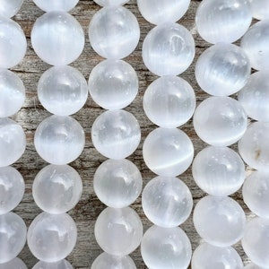 Selenite gemstone strands laid on a pieces of wood in outdoor and photographed under natural light. These beads are semi transparent with some white hues. Selenite beads have chatoyancy effect.closed up photo