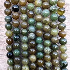 Könnte beinhalten: Eine Strähne runder, grüner und brauner Edelsteinperlen. Die Perlen sind glatt und poliert, mit einer Vielzahl von Grüntönen und Brauntönen.