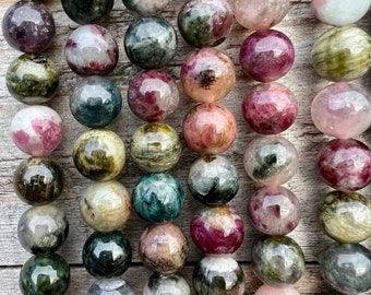 Pode incluir: Um fio de contas redondas de pedras preciosas multicoloridas. As contas são uma mistura de verde, rosa e branco com um padrão salpicado.