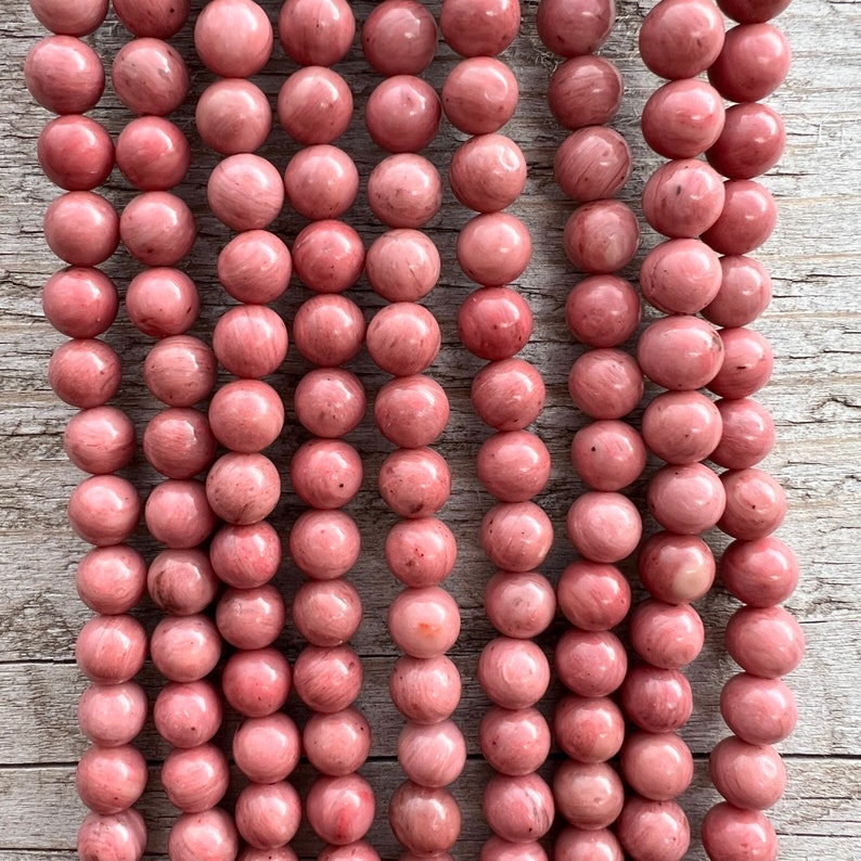 Rhodonite beads strands laid on a bright wooden board in outdoor under natural light. These are round 8mm beads with 1mm hole in middle for threading. they have a very delicate vein on them.