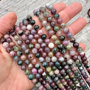 Tourmaline stone 8mm beads strands held in hand over a bright wood board at outdoors and pictured under natural day light