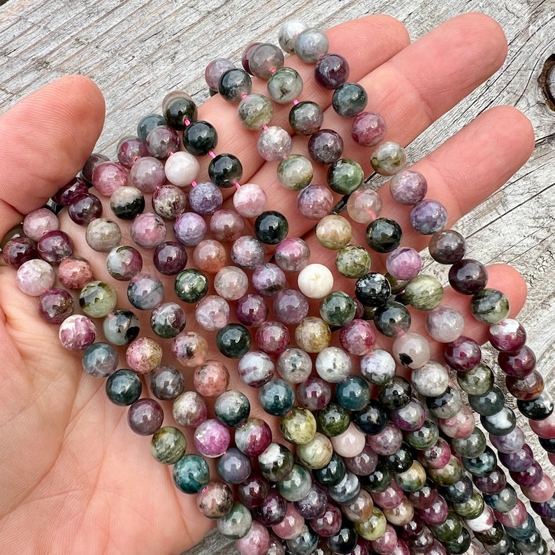 Tourmaline stone 8mm beads strands held in hand over a bright wood board at outdoors and pictured under natural day light