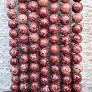 May include: Close-up of numerous round beads in varying shades of red and brown. The beads have a speckled pattern and a shiny surface. These beads are likely for jewellery making or crafts.
