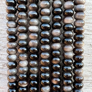 Op de afbeelding: Een streng grijze en zwarte edelsteen kralen. De kralen zijn ovaalvormig en hebben een gladde, gepolijste afwerking.