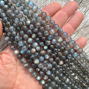 Labradorite stone 8mm beads strands held in hand on a bright wood board in outdoors under natural light.