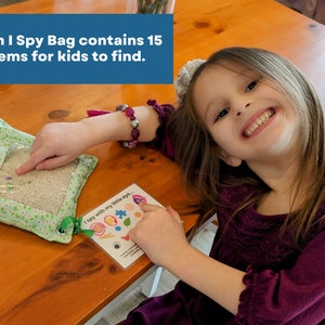 May include: A square fabric I Spy bag with a clear plastic window filled with rice and small hidden objects, accompanied by a white card featuring the text I spy with my little eye and illustrations of fifteen items for kids to find.