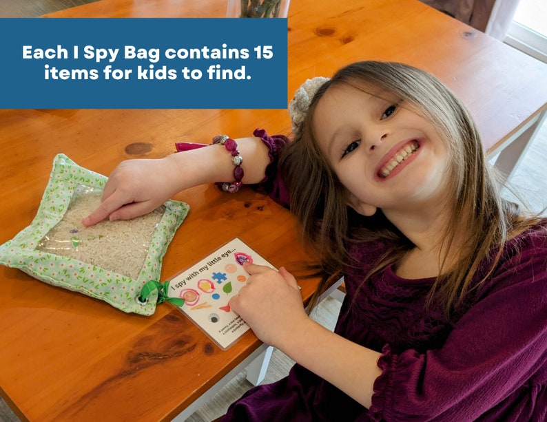 May include: A square fabric I Spy bag with a clear plastic window filled with rice and small hidden objects, accompanied by a white card featuring the text I spy with my little eye and illustrations of fifteen items for kids to find.