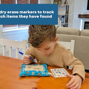 May include: A blue fabric pouch with a clear window containing small objects, accompanied by a card with colorful icons and the text 'Use dry erase markers to track which items they have found' printed on the image overlay.