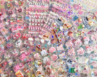 May include: A collection of colorful, transparent stickers featuring various designs. The stickers include images of desserts, bears, hearts, and other cute characters in shades of pink, white, and blue. Some stickers have glitter accents.