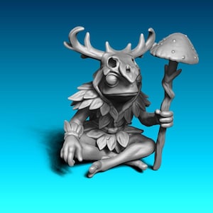 Könnte beinhalten: Graue Figur einer froschartigen Kreatur mit Geweih und blattartigen Kleidungsstücken, die im Schneidersitz sitzt. Sie hält einen Stab mit Pilzaufsatz. Die Figur hat ein skurriles Fantasy-Thema mit detailliertem Design.