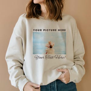 May include: A cream-colored sweatshirt with a photo of a father holding a child in the air. The text "YOUR PICTURE HERE" is above the photo and "Your Text Here!" is below the photo.