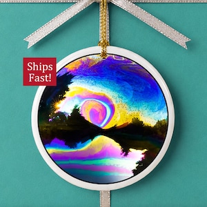 May include: A round white ceramic ornament featuring a vibrant, abstract landscape with swirling colors of blue, purple, yellow, and pink. The design depicts a dark silhouette of trees reflected in water, suspended by a gold cord and a silver ribbon.