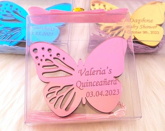 Puede incluir: Tres cajas transparentes con decoraciones en forma de mariposa rosa, azul y dorada. La mariposa rosa tiene el texto "Valeria's Quinceañera 03.04.2023". La mariposa azul tiene el texto "Birthday 1.15.2023". La mariposa dorada tiene el texto "Daphne Baby Shower October 9th, 2023".