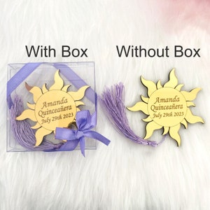 May include: A gold sun-shaped mirror with a purple tassel and the text "Amanda Quincea&ntilde;era July 29th 2023". The mirror is shown in a clear plastic box with a purple ribbon and bow. The mirror is also shown without the box.