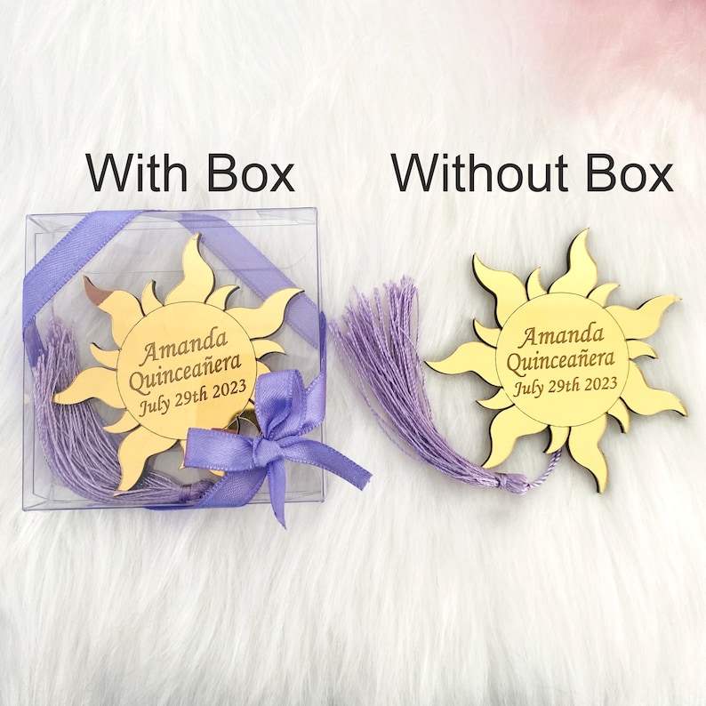 May include: A gold sun-shaped mirror with a purple tassel and the text "Amanda Quincea&ntilde;era July 29th 2023". The mirror is shown in a clear plastic box with a purple ribbon and bow. The mirror is also shown without the box.