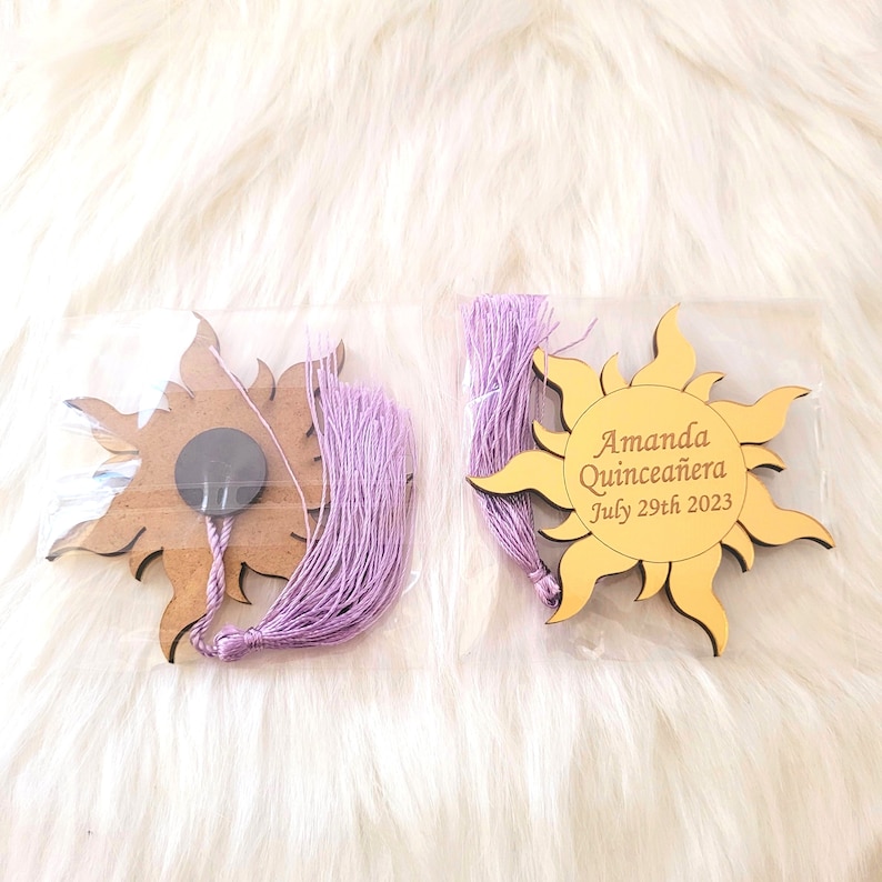 May include: Two wooden sun-shaped ornaments with a purple tassel. One ornament has the text "Amanda Quincea&ntilde;era July 29th 2023".