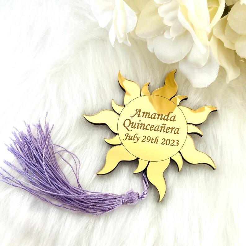 May include: Gold mirror sun with a purple tassel, featuring the text "Amanda Quincea&ntilde;era July 29th 2023".
