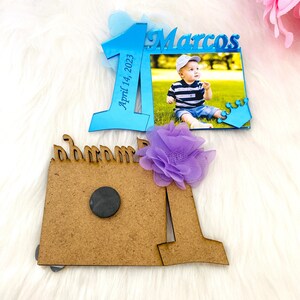 May include: Blue and brown wooden photo frame with a picture of a baby boy. The frame is decorated with a purple flower and a blue crown. The frame says "Marcos" and "April 14, 2023".