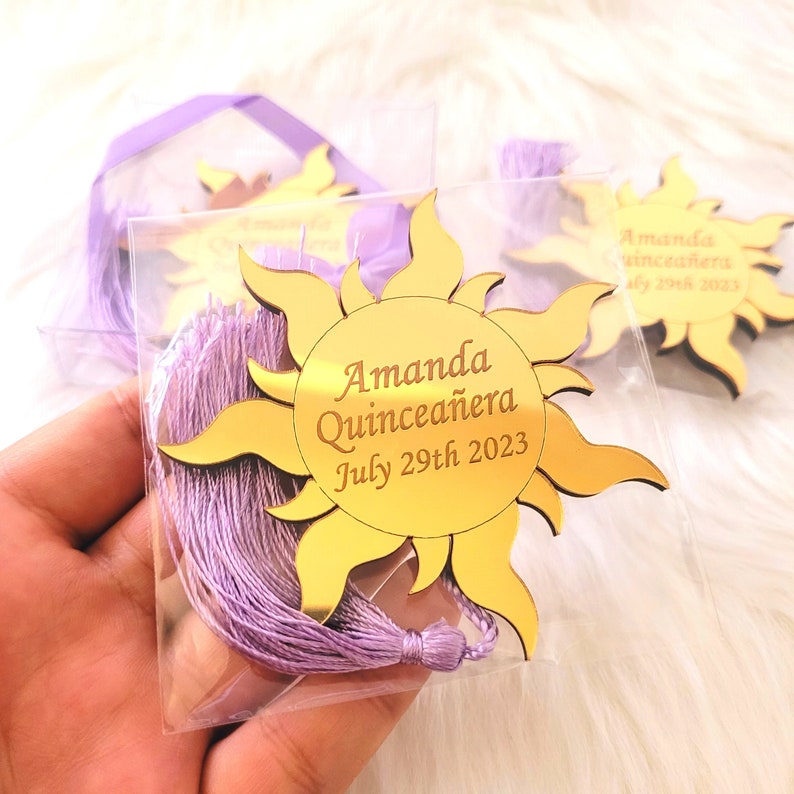 May include: Gold mirror sun with a purple tassel, featuring the text "Amanda Quincea&ntilde;era July 29th 2023".