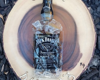 May include: A bottle of Jack Daniel's Tennessee Whiskey on a wooden serving tray with the words "Jack Daniels" and "M&B" inscribed on it.