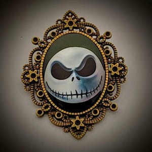 Peut inclure: Broche ovale représentant Jack Skellington de L'Étrange Noël de Monsieur Jack. Le visage du personnage est blanc et bleu, avec des yeux noirs et un sourire cousu. La broche a un cadre en filigrane doré avec des étoiles et des cercles.