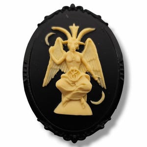Op de afbeelding: Ovale zwarte cameo met een crèmekleurige Baphomet-figuur met vleugels, hoorns en een halve maan. De cameo heeft een decoratief zwart frame. Dit gothic-thema is geschikt voor sieraden of knutselen.
