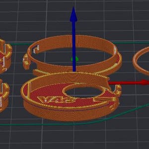 Puede incluir: Una representaci&oacute;n 3D de varios objetos circulares de color naranja y rojo con un agujero central. Los objetos tienen un dise&ntilde;o detallado, con las letras "V43" visibles en algunos. Tambi&eacute;n hay un anillo naranja separado, junto con un contorno verde.