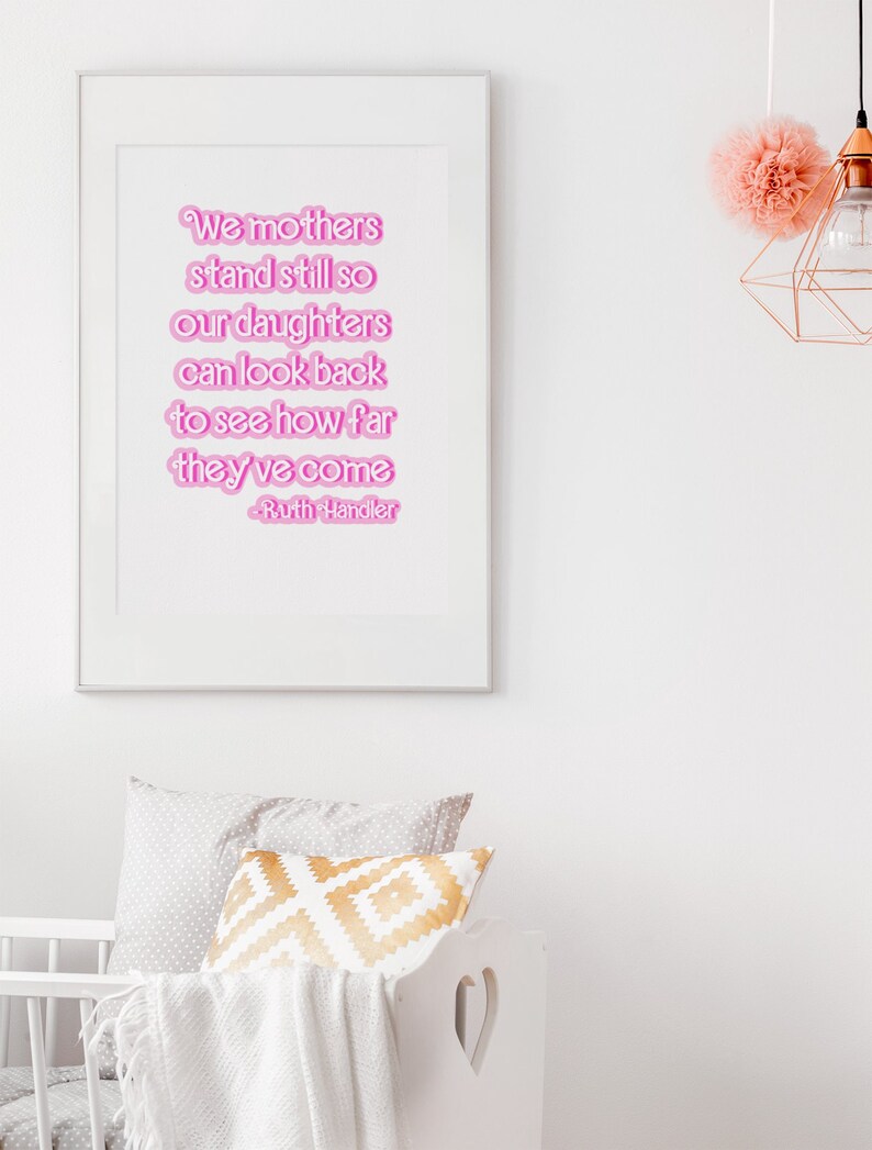 K&ouml;nnte beinhalten: Ein wei&szlig;er gerahmter Druck mit einem rosafarbenen Zitat, das lautet: "We mothers stand still so our daughters can look back to see how far they've come - Ruth Handler".