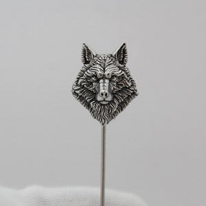 May include: A silver wolf head lapel pin with a detailed design. The pin is attached to a long, thin silver stem.