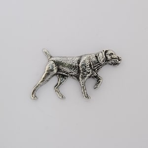 May include: A silver-toned metal brooch shaped like a dog in a walking stance. The piece features a textured, antiqued finish that highlights the canine's muscular build, pointed ears, and short tail, capturing a realistic profile view of the animal.