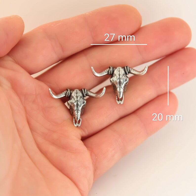 Puede incluir: Dos abalorios de plata con forma de cr&aacute;neo de toro, cada uno mide 27 mm de ancho y 20 mm de alto. Los abalorios tienen un dise&ntilde;o detallado con cuernos y una superficie texturizada.