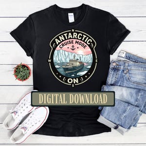 May include: Black t-shirt with a circular graphic featuring a cruise ship sailing in icy waters under a pink and blue sky. The graphic reads "Antarctic Cruise Mode On" with an anchor and compass rose design. The words "Digital Download" are on a rectangular label.