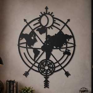 Può includere: Un'opera d'arte da parete in metallo nero che presenta una silhouette circolare di una mappa del mondo integrata con un design a bussola. L'opera include una luna crescente in alto, una rosa dei venti in basso e frecce rivolte verso l'esterno.