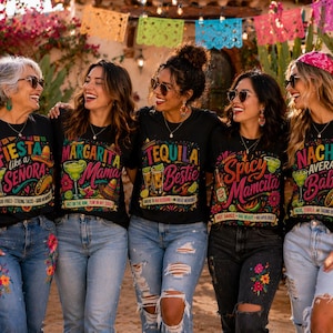 May include: A group of five people wearing black t-shirts with vibrant graphics and text. The shirts feature phrases such as "Tequila Bestie" and "Nacho Average Babe." They are smiling and wearing sunglasses, standing outdoors with colourful decorations.
