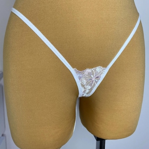 Op de afbeelding: Witte kantenlingerie met een bloemenpatroon. De lingerie is op een mannequin.