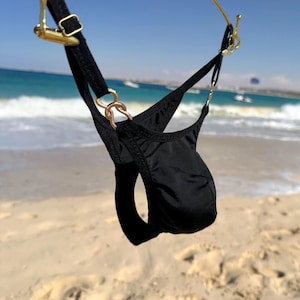 Può includere: Uno slip da bagno a perizoma nero con sottili cinturini neri e connettori in metallo color oro. Il capo presenta un design a sacca frontale sagomata con cursori laterali regolabili e una costruzione minimalista per un aspetto elegante.