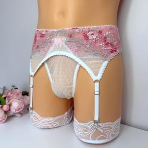 Può includere: Un reggicalze a vita alta in rete bianca trasparente a pois, impreziosito da un intricato ricamo floreale rosa e bianco lungo il bordo superiore. Il capo presenta spalline bianche regolabili e bordi in pizzo bianco sulle aperture.