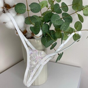 Puede incluir: Lencer&iacute;a de encaje blanco con un dise&ntilde;o floral. La lencer&iacute;a es delicada y transparente, con un delicado patr&oacute;n floral.
