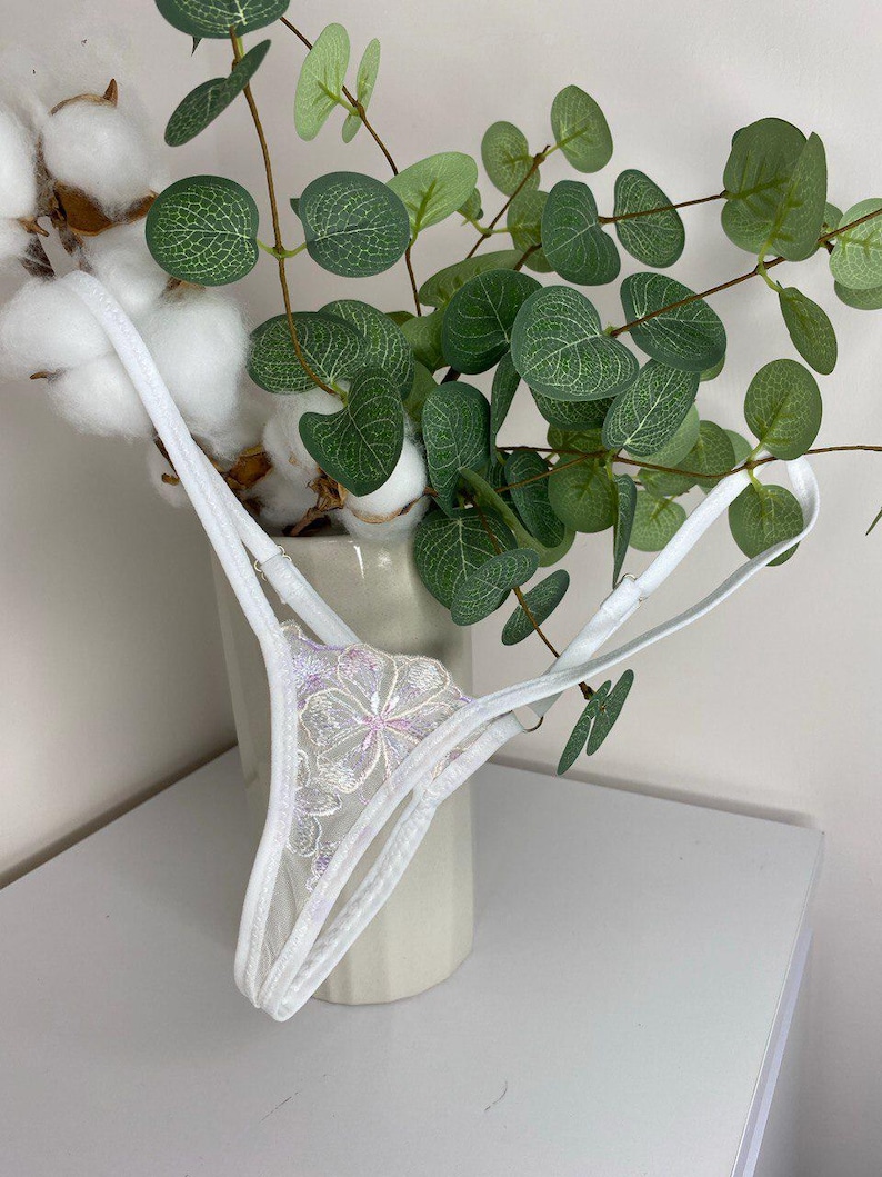 Puede incluir: Lencer&iacute;a de encaje blanco con un dise&ntilde;o floral. La lencer&iacute;a es delicada y transparente, con un delicado patr&oacute;n floral.