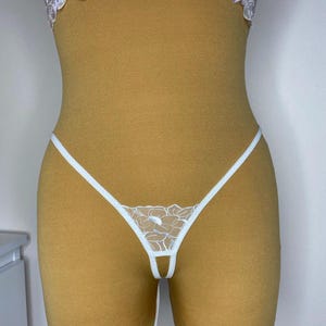 May include: White lace lingerie with a floral design. The lingerie has a small opening in the front.